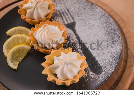 Homemade Lemon tarts with meringue on black plate.