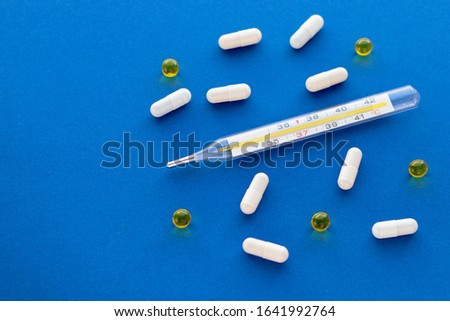 Mercury thermometer, jelly pills and white capsules isolated on blue background. Epidemic, painkillers, healthcare and treatment concept. Flat lay. Top view with copy space.