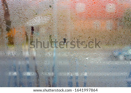 Condensation water drops on a window with a background of regular street with cars and houses