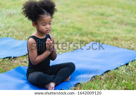 African american little girl sitting on the roll mat practicing meditate yoga in the park outdoor Royalty-Free Stock Photo #1642009120