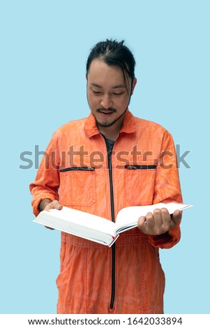 The chief mechanic in an orange uniform holding big book. Stand and read the maintenance manual carefully. Portrait with studio light.