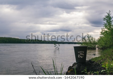 Paper Cup with a wish for a good day on the background of the river.