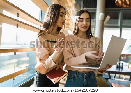 twins sisters work with laptop and notice something in notebook