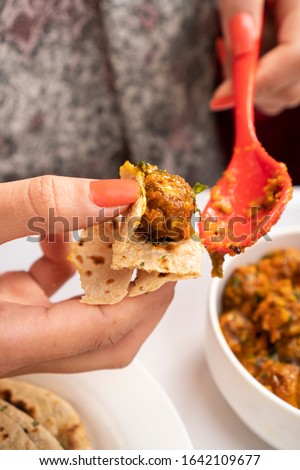 Close-up of woman hand taking a food bite and eating chapatti (roti) with Potato curry (Kashmiri dum aloo).