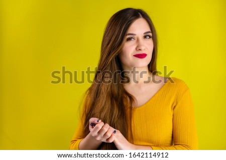nice brunette girl with long hair with a smile in a yellow jacket rejoices on a yellow background, smiles and shows positive emotions