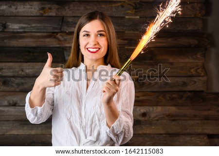 nice brunette girl with long hair with a smile in a white shirt laughs merrily with a burning fire clapper in her hands on a wooden background showing positive emotions