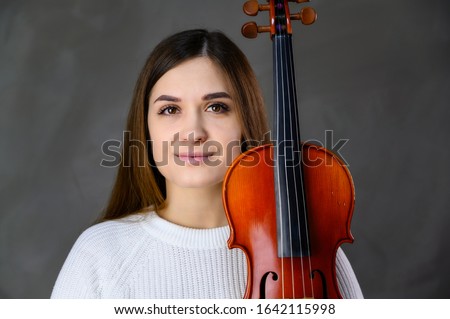 Concept musician violinist. Portrait of a pretty brunette girl in a white sweater playing the violin on a gray background