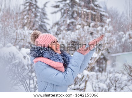 A young girl plays snowballs in a snowy park. Photo in pastel pink and blue tones.