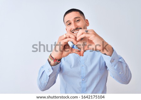 Young handsome business man standing over isolated background smiling in love doing heart symbol shape with hands. Romantic concept.