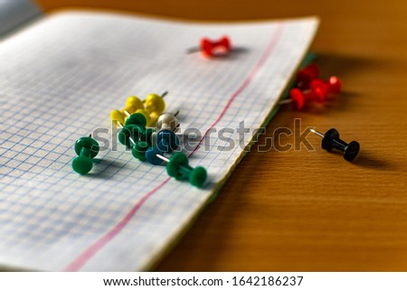 Colored small office buttons with different convenient protective hats, modern office details scattered on notebook leaves in a check
