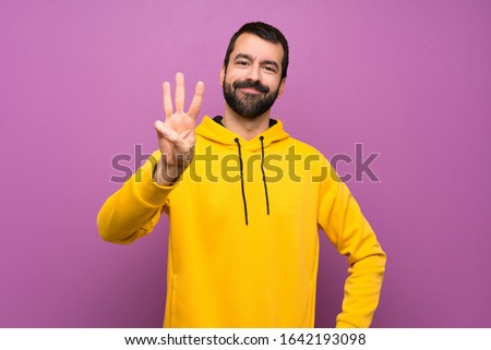 Handsome man with yellow sweatshirt happy and counting three with fingers