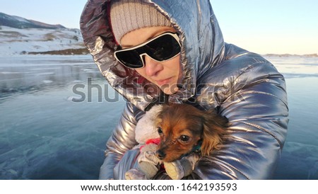 Toy Terrier in funny clothes and funny shoes plays with ball on beautiful ice in cracks. Mom and daughter in sports clothes and figure skates. Girls throw toy to dog. Doggy catches up favorite toy.