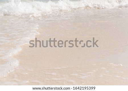 Soft white foam on sea water surface wave ripple on the sand in closeup