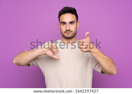 Young handsome man over isolated purple background making good-bad sign. Undecided between yes or not
