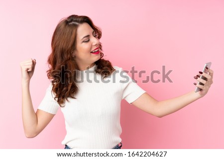 Young Russian woman over isolated pink background taking a selfie with the mobile