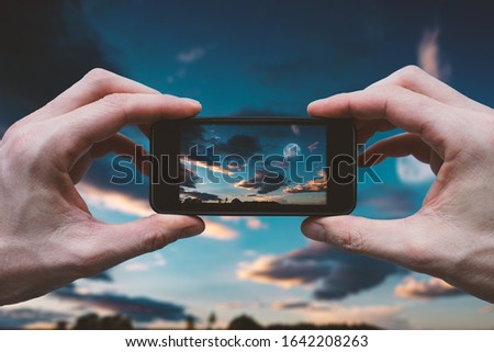 Hands Holding Mobile Phone - Camera and Taking Picture of Moon on Dark Sky with Clouds