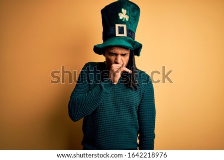 Young african american man wearing green hat with clover celebrating saint patricks day feeling unwell and coughing as symptom for cold or bronchitis. Health care concept.