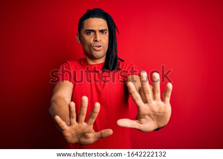 Young handsome african american afro man with dreadlocks wearing red casual t-shirt Moving away hands palms showing refusal and denial with afraid and disgusting expression. Stop and forbidden.