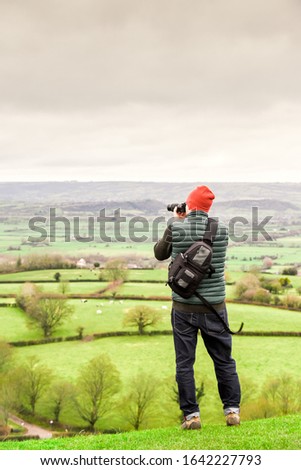 A man looks out over hills to take a photograph during an adventure walking trip