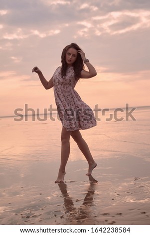 Portrait of a young beautiful bright girl in a summer dress laughing and walking in the sunset on the coast