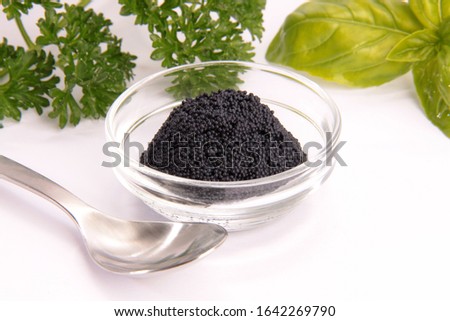 black caviar in a class bowl on white background with garden herbs