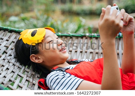 Thai little girl wearing cartoon lion mask laying on a cot playing smartphone with happiness expression.