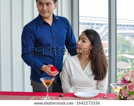 The asian young man proposed the beautiful woman for marry with the engagement ring in red heart box at the romantic dinner table in Valentine festival 