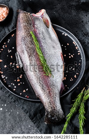 Raw whole trout fish without a head, with salt and rosemary. Black background. Top view