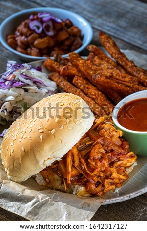 Vegan Jackfruit barbecue on a bun with baked bbq beans and baked sweet potato fries. Close up.