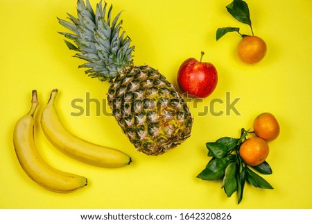 top view fresh tropical fruits layout pineapple,bananas, apple and tangerines on a yellow background 