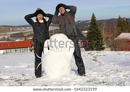 A couple have built a snowman. A woman and a man built an Enton out of snow