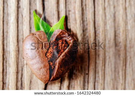 Heart shaped coffee bean with green leaves on old wooden background. Close-up. Coffeemania.