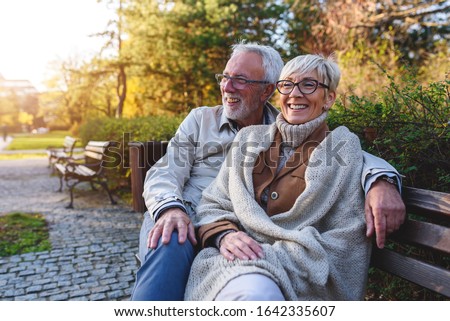 Smiling senior couple sitting on the bench in the park together enjoying retirement Royalty-Free Stock Photo #1642335607