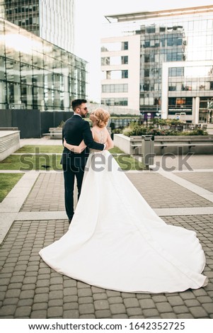Brides at photo shoots near glass structures, business center.
Young dress with long white plume, groom in black tuxedo and  sunglasses