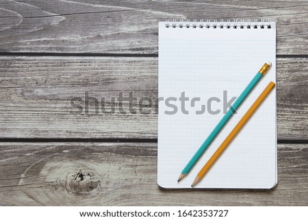 Notepad with a blank white sheet in a checker paper with two simple graphite pencil lies on the background of wooden boards