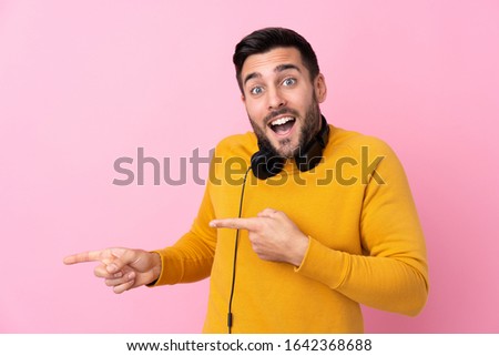 Young handsome man with earphones over isolated pink background surprised and pointing side