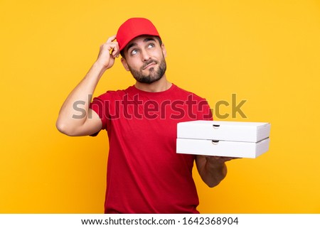 pizza delivery man with work uniform picking up pizza boxes over isolated yellow background having doubts and with confuse face expression