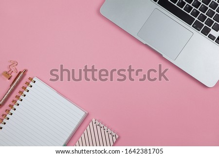 Modern female working space, top view. Laptop, notebooks, pen, clamp on pink backround, copy space, flat lay. Desktop of freelancer. Work from home concept. Horizontal.