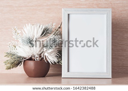 Photo frame and white flowers on a light wooden background, place for text.