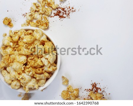 top view of barbecue popcorn in white bowl on white background with popcorn and chilli powder on the white floor. picture with space for text.