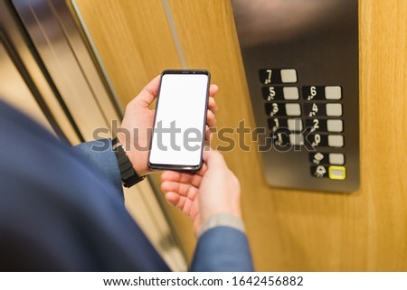 Close up of businessman using blank screen smartphone in elevator. Business and office building meeting concept.