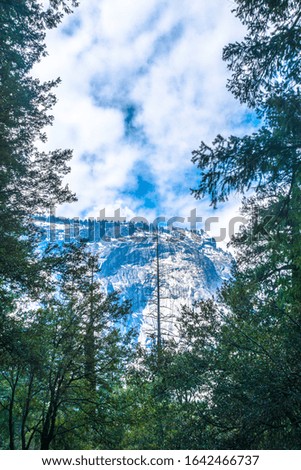 Snow-covered mountain behind trees seen hiking on Mist Trail in Yosemite National Park. Royalty free stock photo.