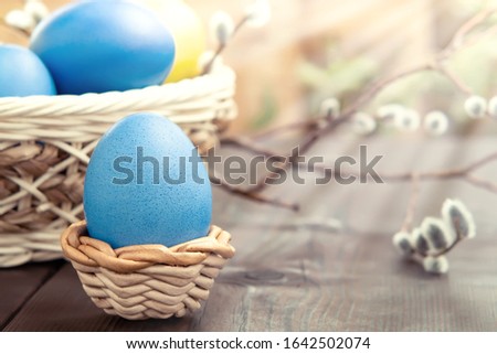 Easter composition - several colored eggs in a basket and on a dark wooden table with willow twigs
