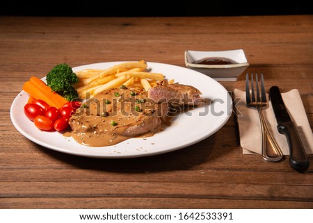 Big steak, french fry, pepper, little tomato, slice carrot, broccoli and BBQ sauce with fork, knife, tissue paper on wood table stock photo