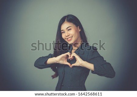 a beautiful woman  makes heart shape with fingers, hands, isolated on Gray wall background. Positive human emotion facial expression feeling body language attitude