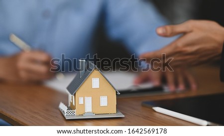 Cropped shot of Real estate agent offer house insurance or house ownership to smart man in blue shirt at the modern wooden table. Signing on agreement, Broker/Seller/Dealer concept.