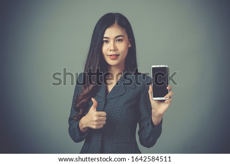 A portrait of a beautiful woman holding on her smart phone on gray bckground.