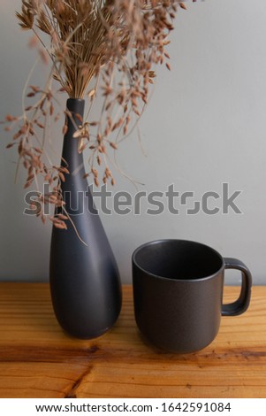 Mockup of a black coffee or tea cup that stands on a wooden table with dried flowers in a vase.