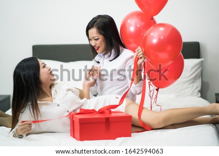 Beautiful young woman and his friend with balloons red and box on bed. Valentine's day celebration