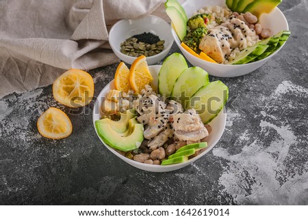 Close up Buddha bowl with chicken meat, bulgur, white beans, quinoa, avocado, lemon and fresh cucumber.